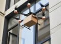 Capturing the essence of futuristic delivery services, this photo shows a sophisticated drone in the midst of a delivery operation. Outfitted with multiple rotors for stability and precision, the drone deftly hovers outside an apartment building, carefully holding a package likely containing goods ordered online. The building's sleek, modern design juxtaposes the buzzing technology, highlighting the seamless integration of advanced delivery systems into our urban landscapes. This snapshot represents a world where convenience and efficiency take flight, quite literally, and offers a glimpse into the evolution of logistics and commerce in an increasingly digital and automated era.